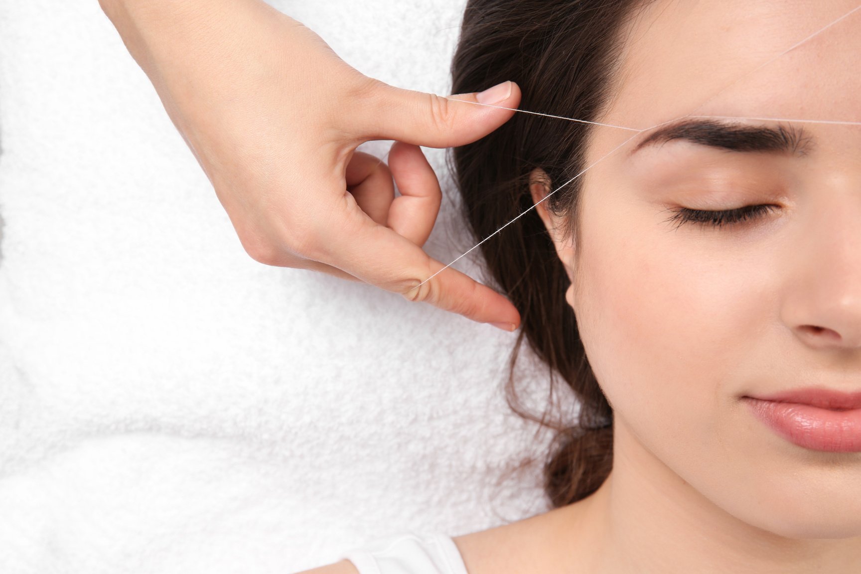 Young Woman Having Professional Eyebrow Correction Procedure in Beauty Salon, Closeup